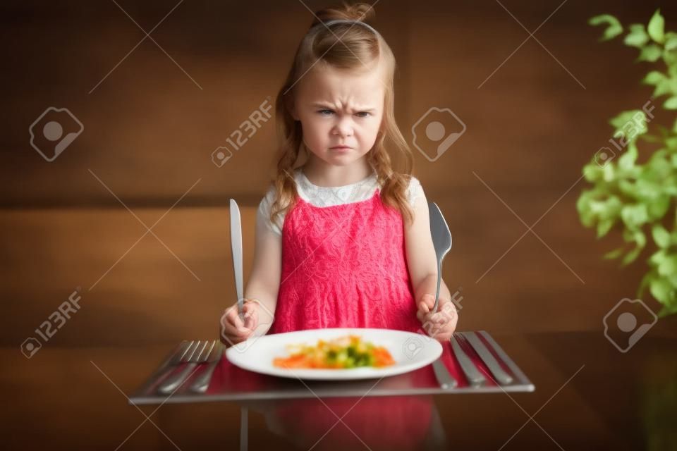 夕食を待っている激怒小さな女の子。フォークを手に持つ
