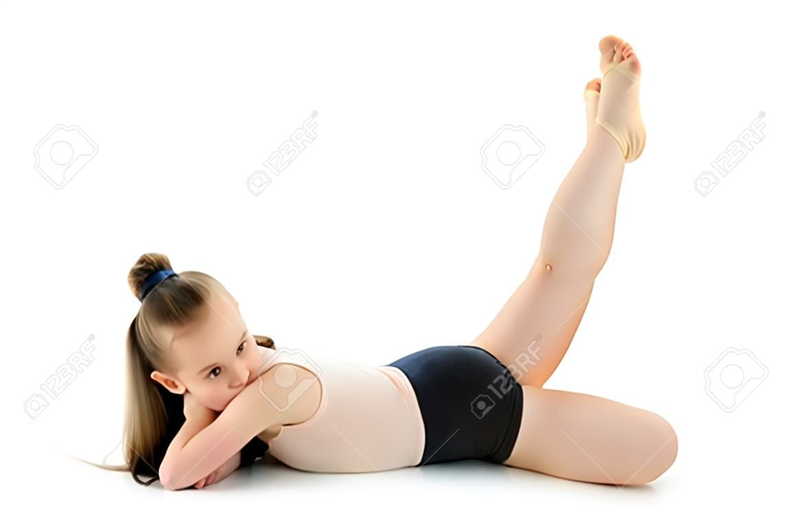Маленькая гимнастка выполняет на полу акробатический элемент.