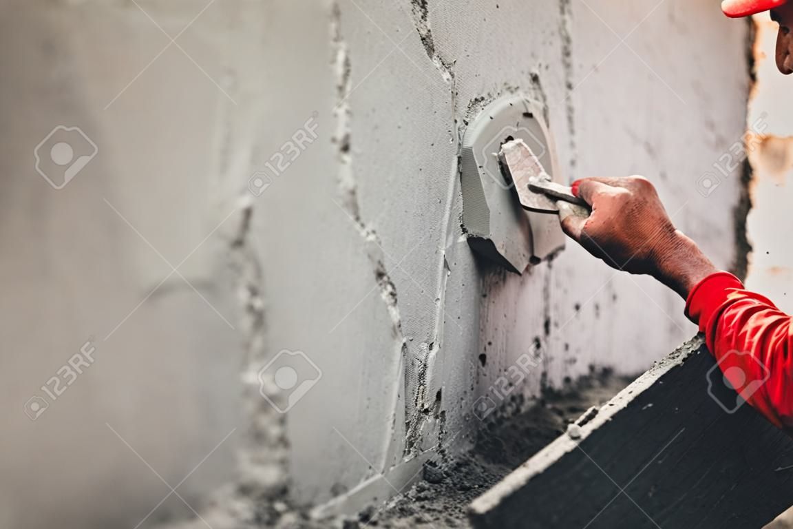 main de travailleur plâtrant du ciment au mur pour la construction d'une maison sur un chantier de construction