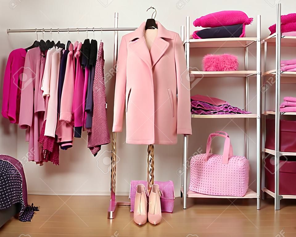 Dressing closet with pink clothes arranged on hangers and shelf, a coat on a mannequin. Fall winter wardrobe full of all shades of pink clothes, shoes and accessories.