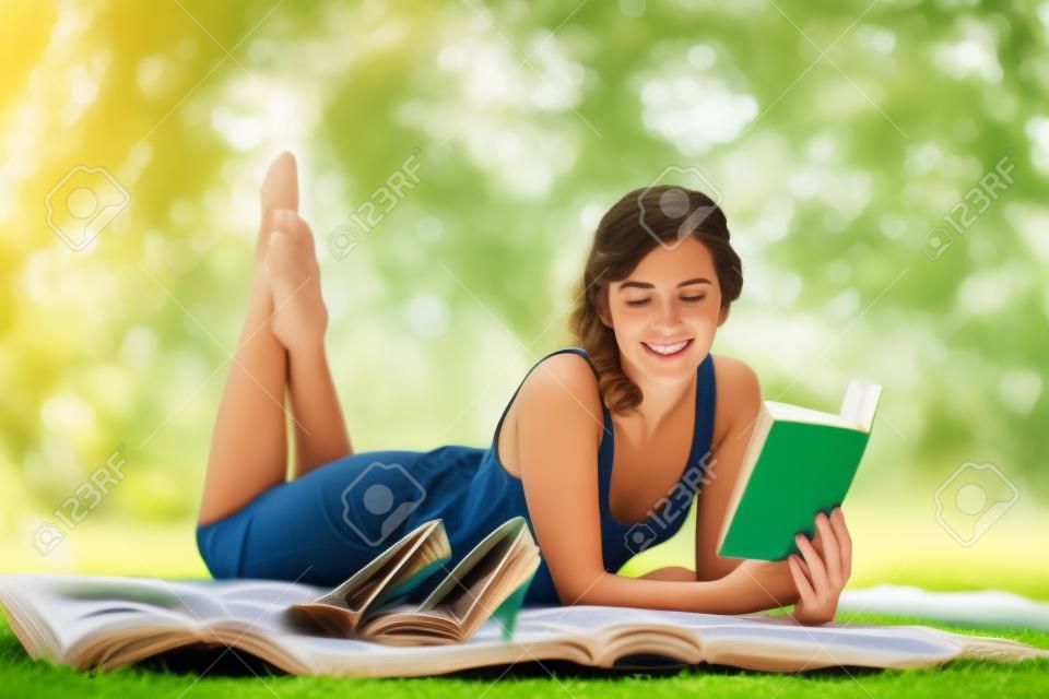 Porträt einer schönen jungen Frau, ein Buch zu lesen, während man auf grünem Gras