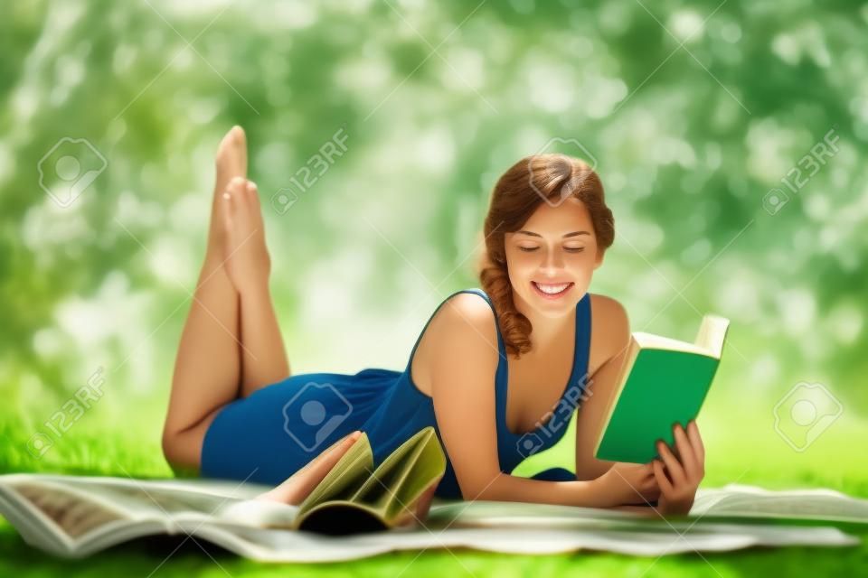 Porträt einer schönen jungen Frau, ein Buch zu lesen, während man auf grünem Gras