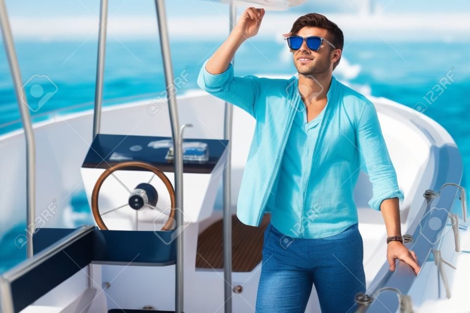 豪華なヨットで海を見ているサングラスをかけたハンサムな若い男。ウォータースポーツ休暇、夏の屋外。休日、レジャー、ライフスタイルのコンセプト