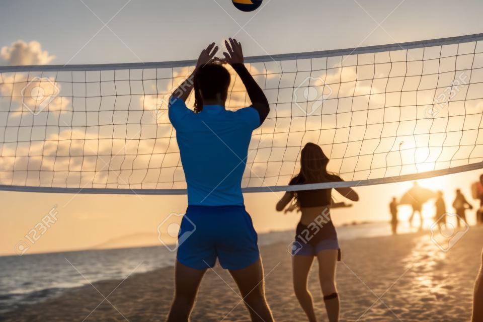 A young couple is playing the volleyball on the beach while sun is setting on a beautiful summer day. Sport, sea, beach