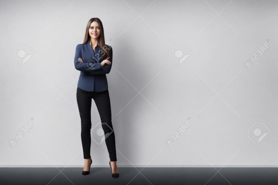 Portrait of young beautiful business woman standing against white wall.