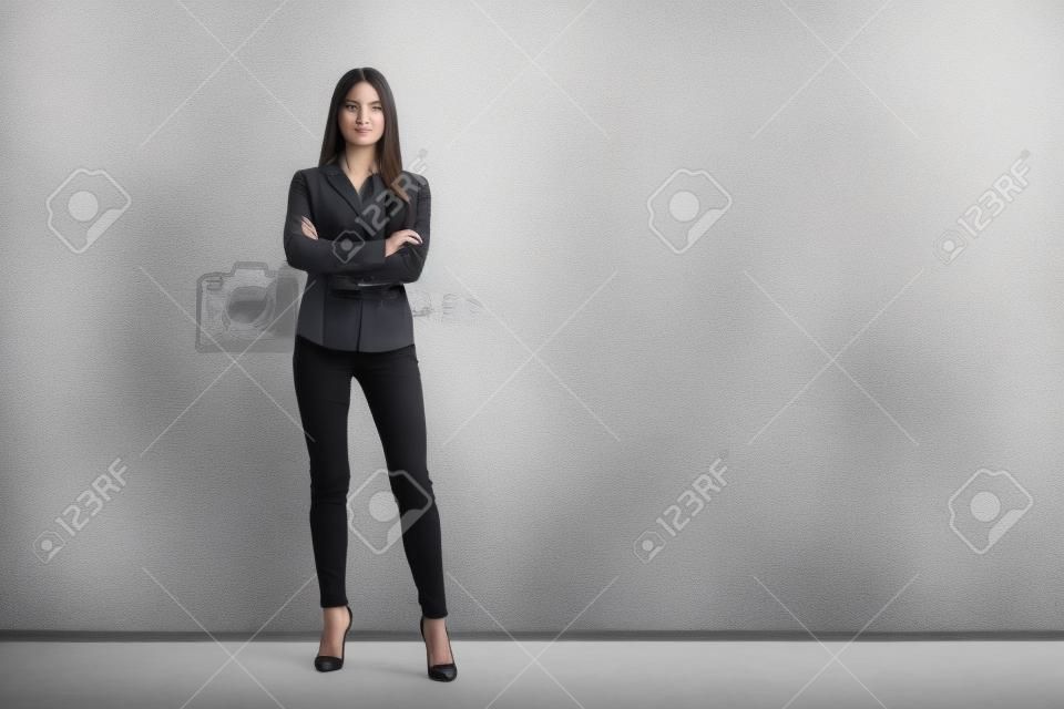 Portrait of young beautiful business woman standing against white wall.