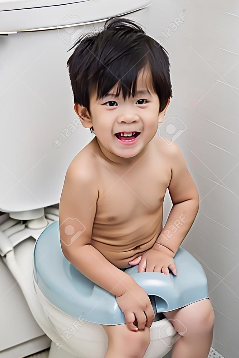 Niño asiático lindo en el estilo moderno inodoro.
