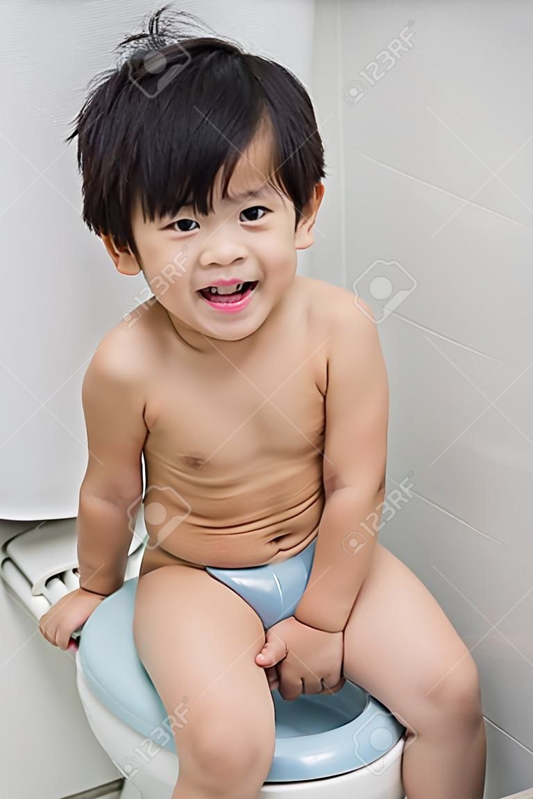 Niño asiático lindo en el estilo moderno inodoro.
