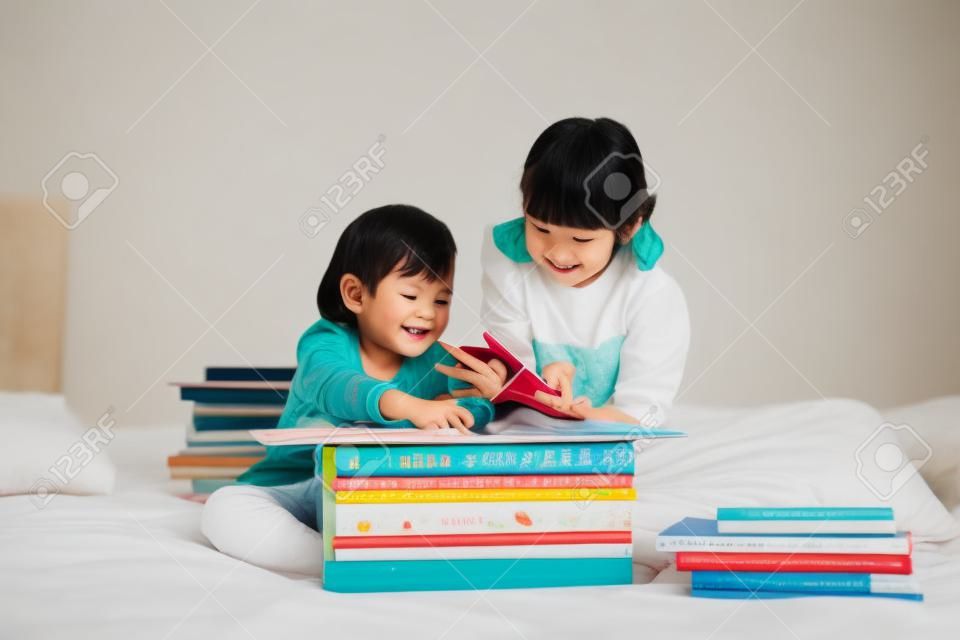 Cute asian children reading a book on white bed