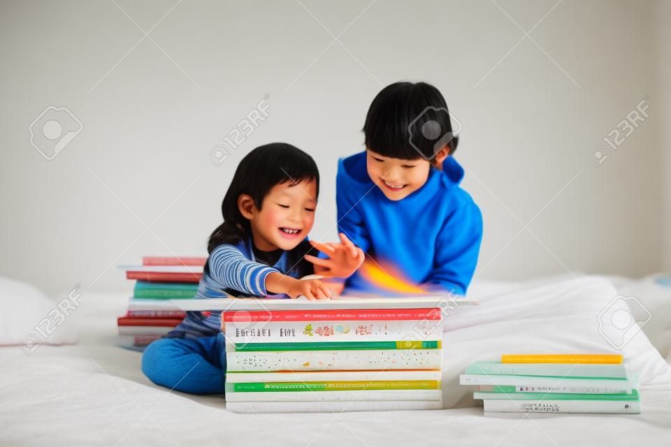 Niños asiáticos lindos de leer un libro en la cama blanca