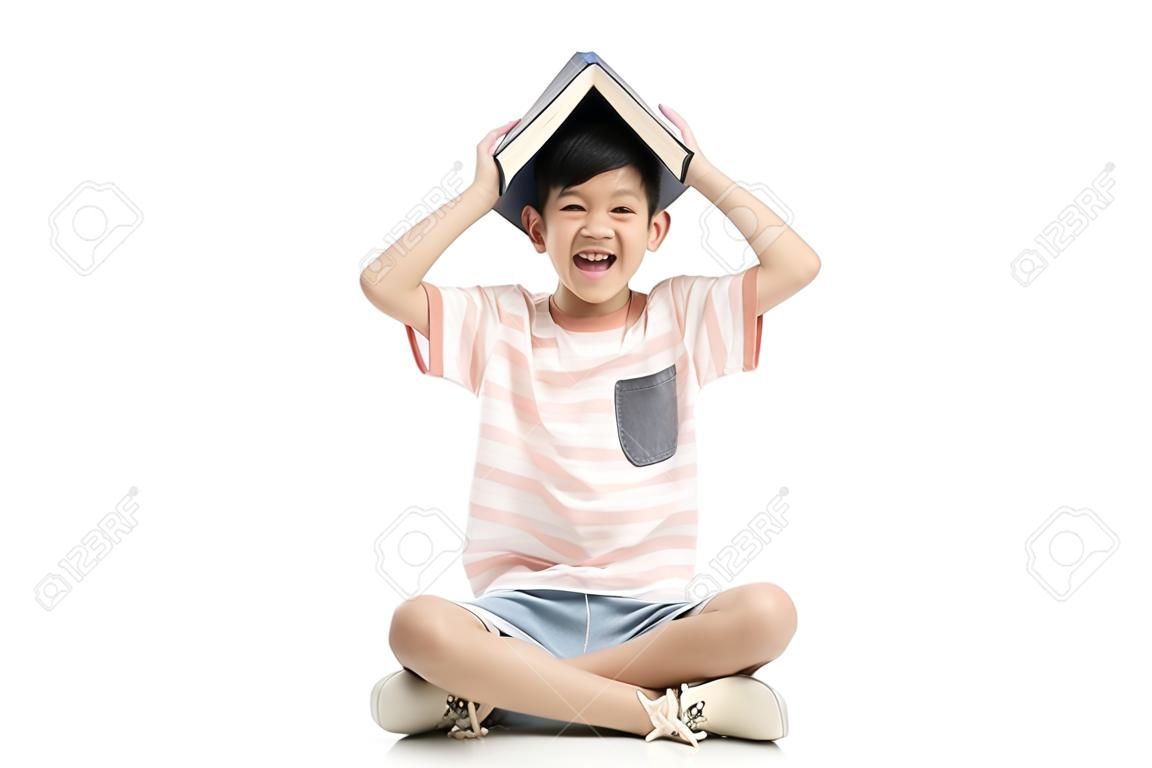 Netter asiatischer Junge mit Buch auf Kopf auf weißem Hintergrund lokalisiert