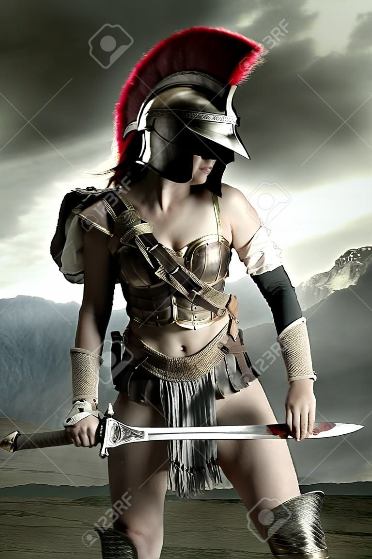 Starożytna wojowniczka lub gladiatorka pozuje na zewnątrz z mieczem i hełmem