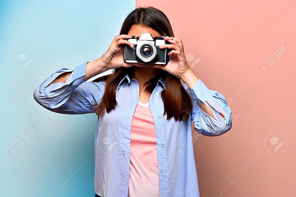 Mujer joven sobre pared rosa y azul sosteniendo una cámara
