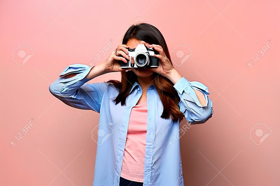 Mujer joven sobre pared rosa y azul sosteniendo una cámara