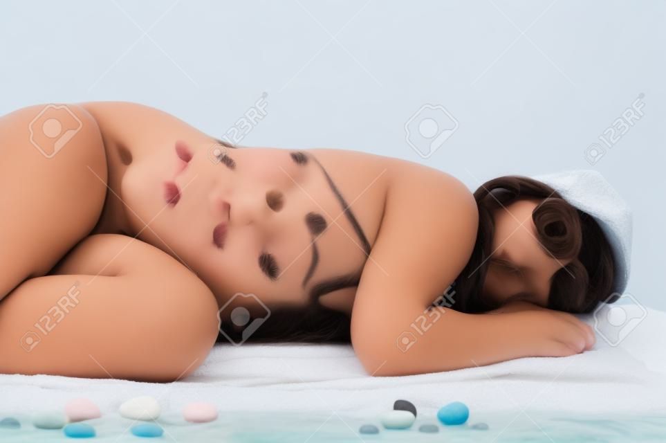 schöne Brünette Mädchen im Teenageralter im Badeanzug Schlafen am Strand (Studio-Einstellung mit Handtuch und Kies, isoliert auf weißem Hintergrund)