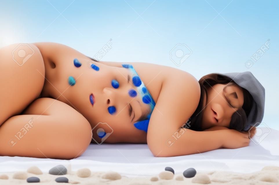 Красивая брюнетка девушка в купальнике спать на пляже (установка студии с полотенцем и гальки, изолированных на белом фоне)