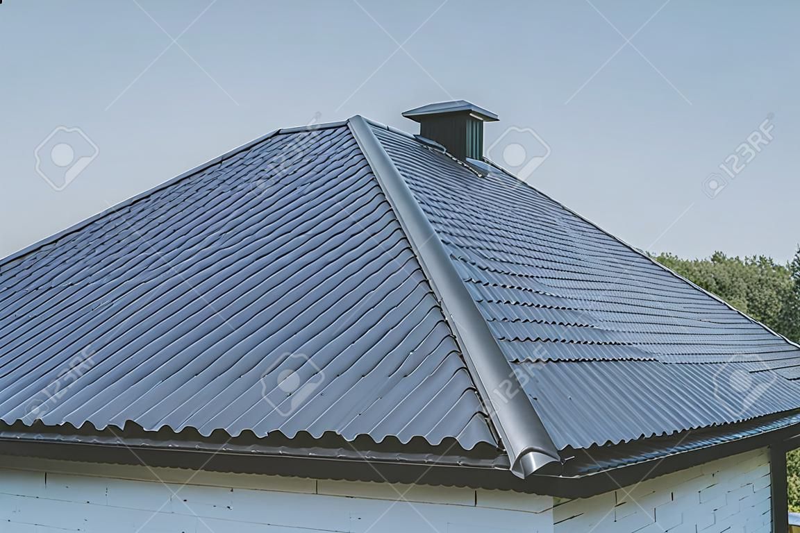Modern roof made of metal. Gray-blue metal roof tiles on the roof of the house. Corrugated metal roof and metal roofing.