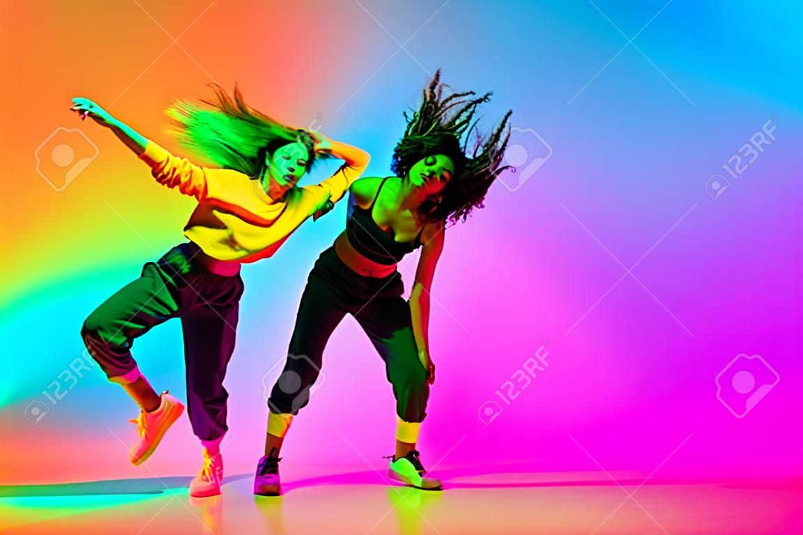 Twee mooie hip-hop meisjes dansen op gradiënt blauw oranje achtergrond in neon