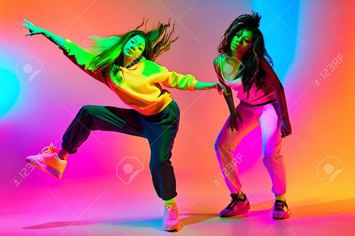 Twee mooie hip-hop meisjes dansen op gradiënt blauw oranje achtergrond in neon