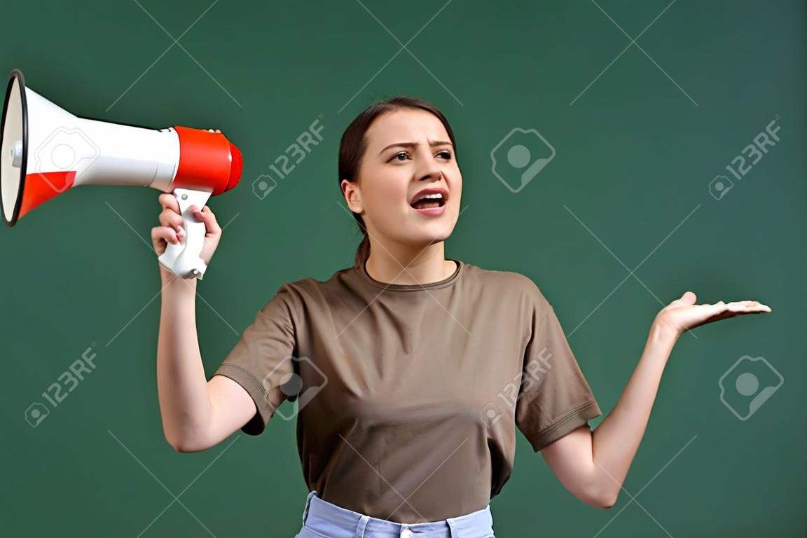 Cropped portrait of young beautiful woman in casual cloth talking in megaphone isolated over green background