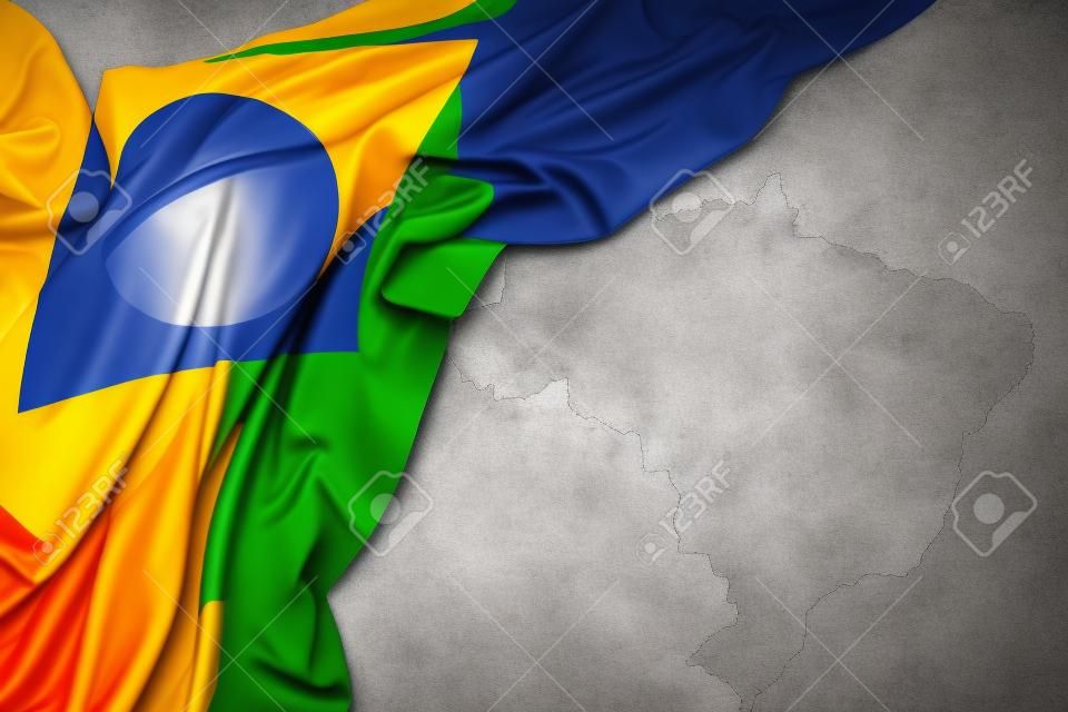 waving colorful national flag of brazil on a gray map background.