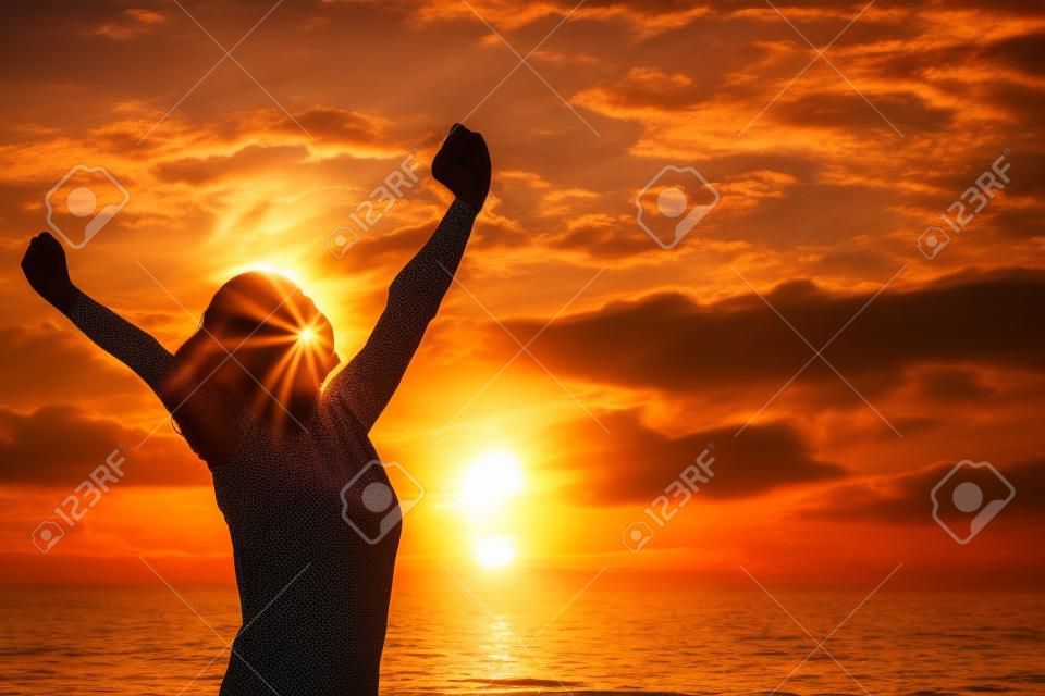 donna forte fiducia braccia aperte sotto il sorgere del sole in riva al mare
