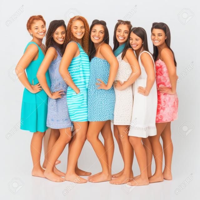 Un portrait de sept copines, debout dans une rangée et souriant sur fond blanc