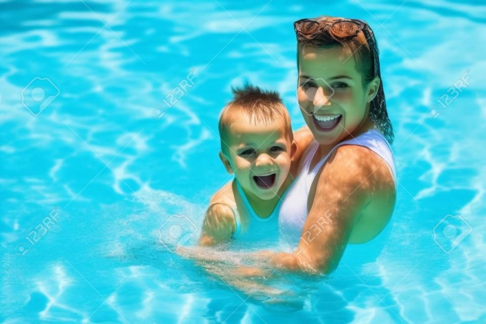 Chico lindo con su madre jugando en la piscina durante el verano