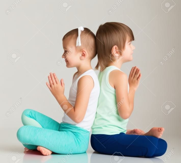 Niño pequeño lindo y práctica de la muchacha de la yoga. Aislado en el fondo blanco