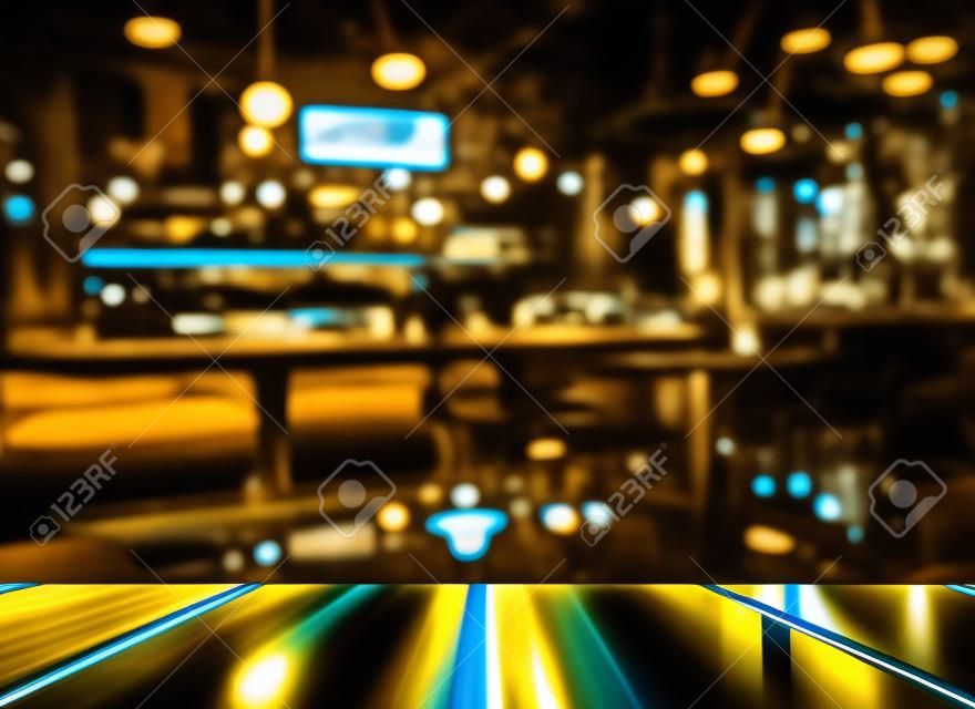 木桌的頂部與光反射與黃色抽像模糊酒吧或俱樂部在漆黑的夜晚背景