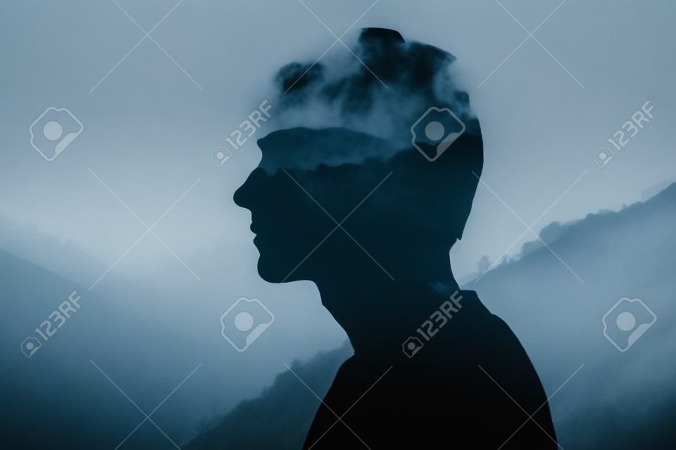 Silhouette of a man looking at the mountains and trees in the fog