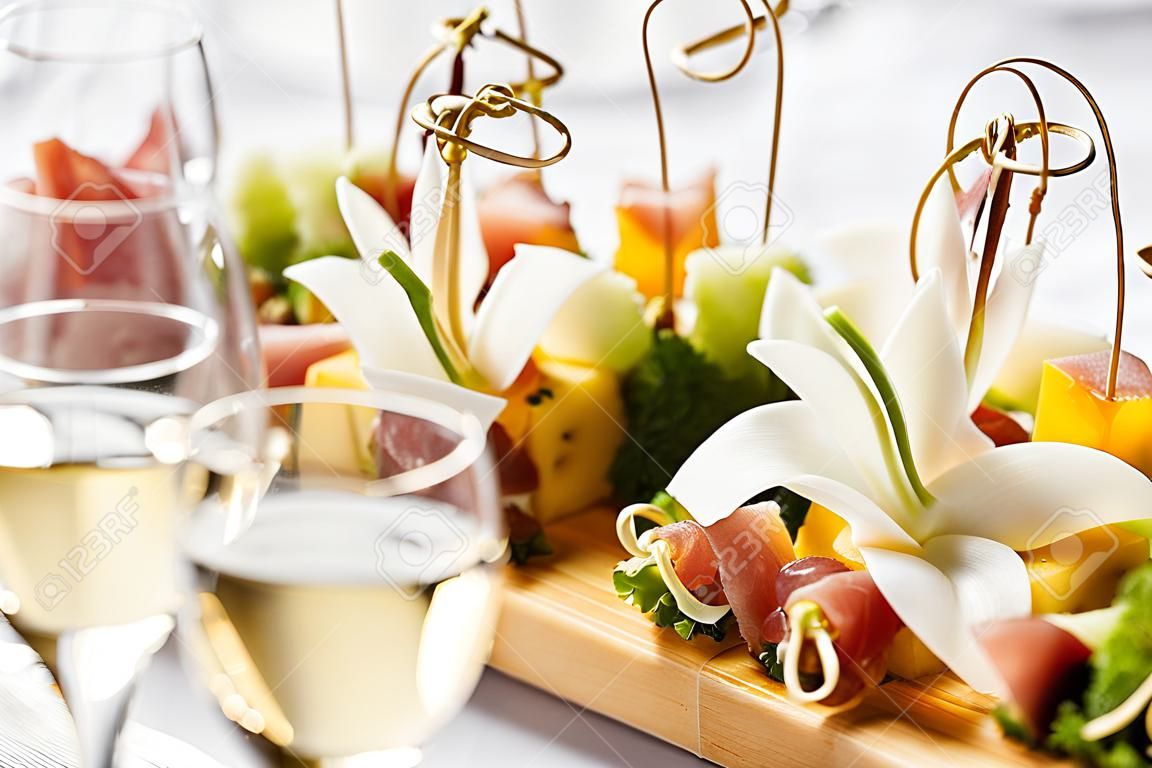 the buffet at the reception. Assortment of canapes on wooden board. Banquet service. catering food, snacks with cheese, jamon, prosciutto and fruit
