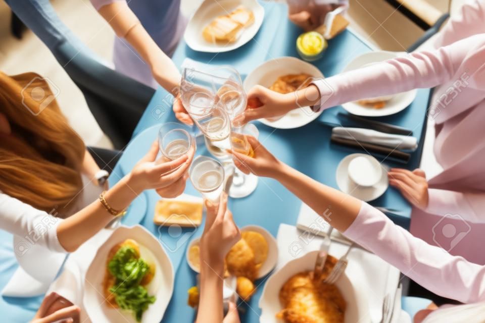 Tintineo de vasos. cinco mujeres Retrato de jóvenes desayunando en la mesa del restaurante. Champán para el desayuno. Habla y ríe, comunicación en vivo