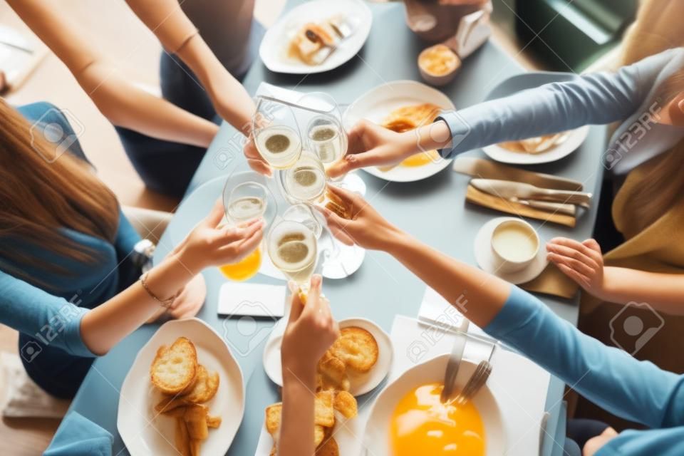 Clink glasses. Five women. Portrait of young people having breakfast at table in restaurant. Champagne for Breakfast. Talk and laugh, live communication