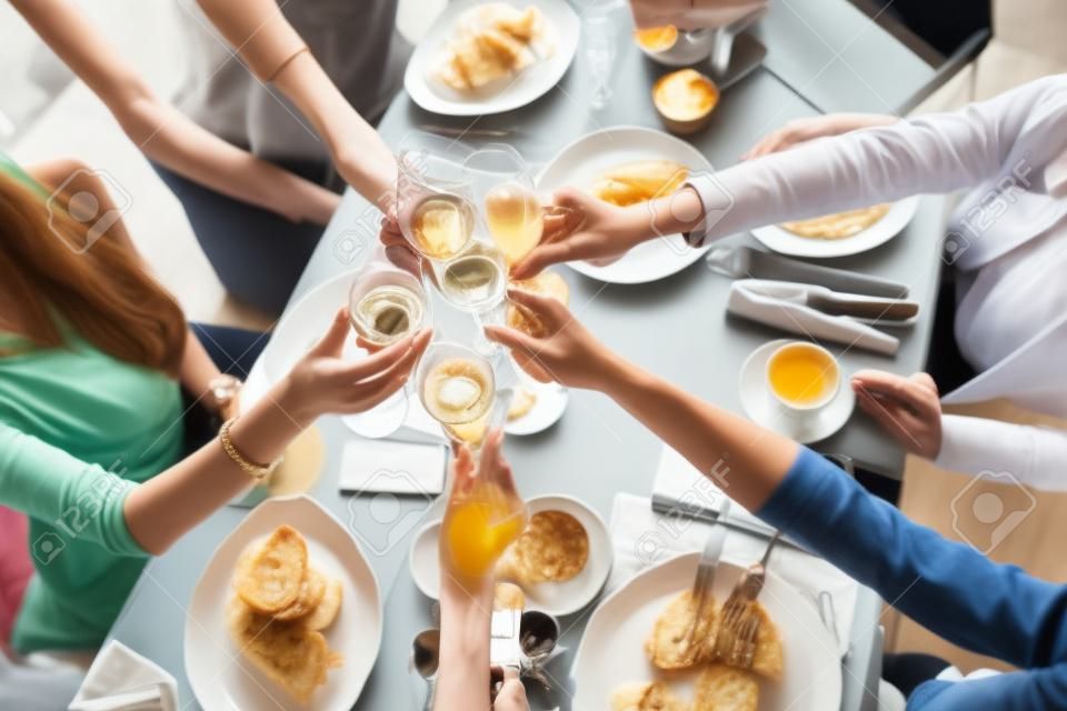 Tintineo de vasos. cinco mujeres Retrato de jóvenes desayunando en la mesa del restaurante. Champán para el desayuno. Habla y ríe, comunicación en vivo