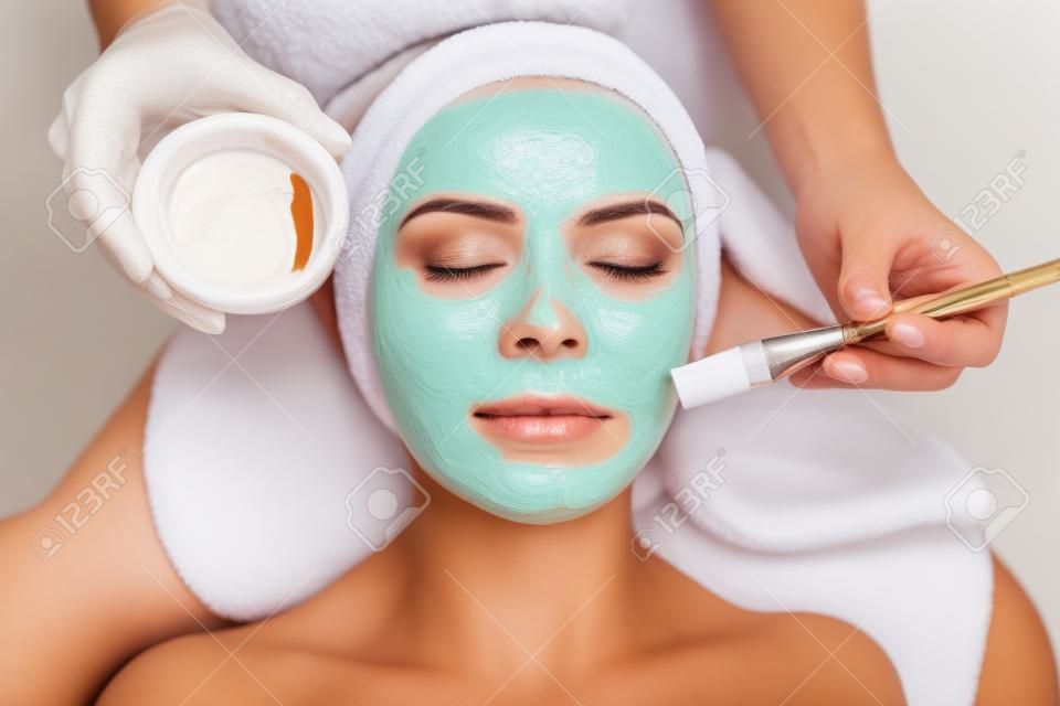 Close-up shot of a woman getting facial treatment with clay mask. Cosmetology and spa