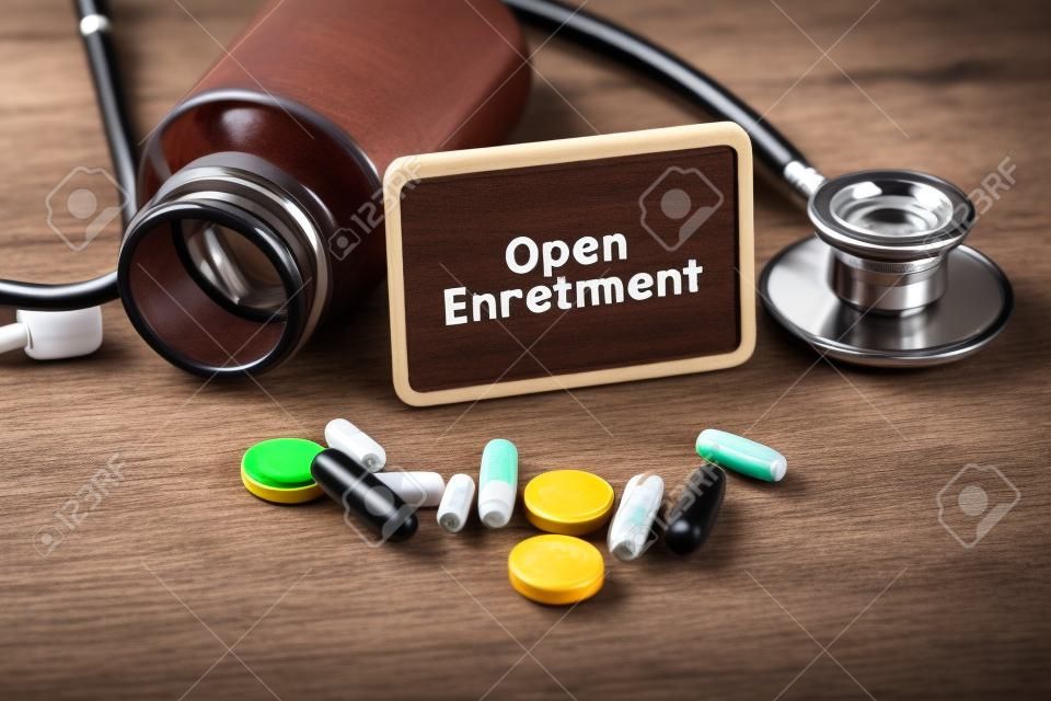 Stethoscope, pill bottle, Various pills, capsules and Open Enrollment on wooden background with copyspace area.