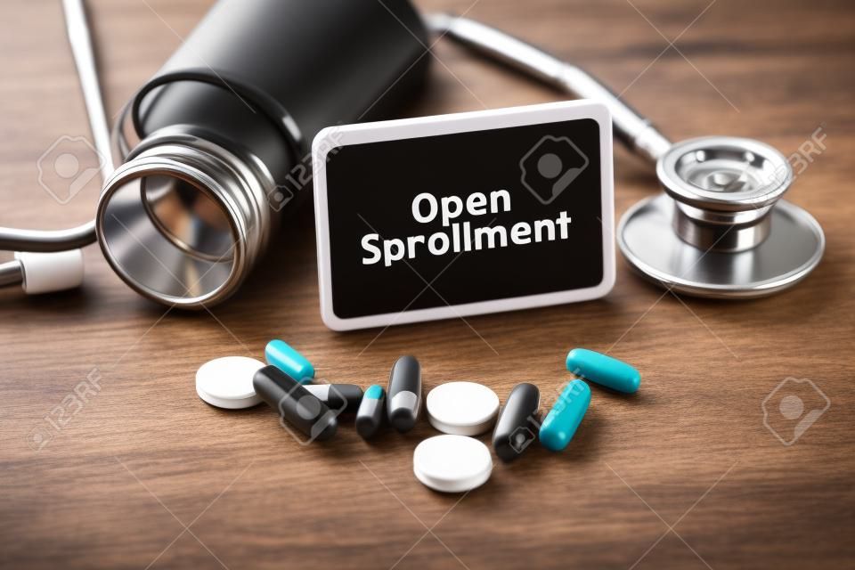 Stethoscope, pill bottle, Various pills, capsules and Open Enrollment on wooden background with copyspace area.