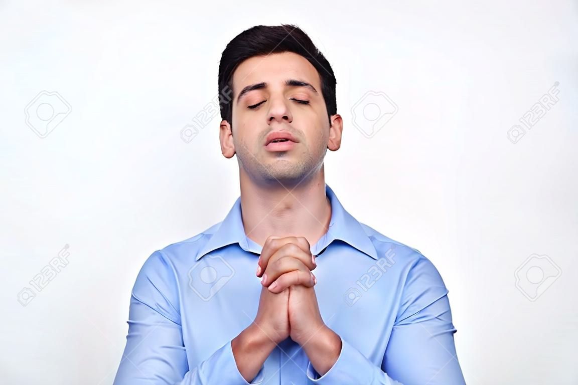 Jovem homem atraente orando com as mãos cerradas