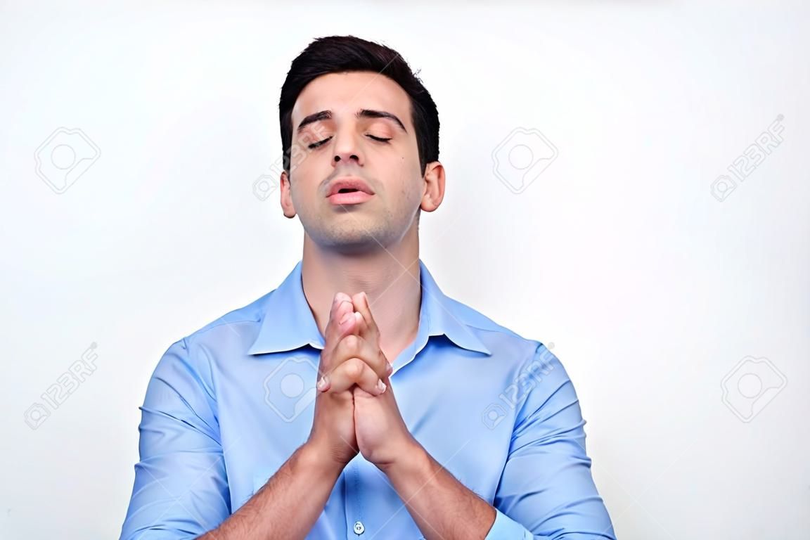 Jovem homem atraente orando com as mãos cerradas