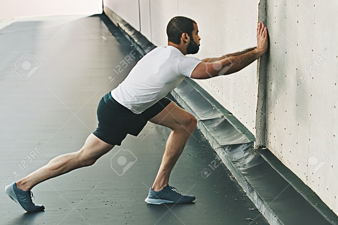 Sterke man Stretching Calf en Leaning op de muur