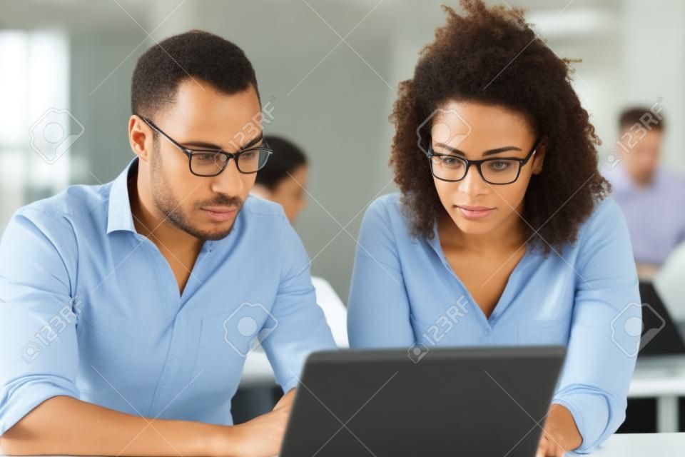 Vários colegas assistindo conteúdo no laptop juntos. Jovem homem e mulher usando computador no escritório, olhando para a tela e conversando. Conceito de discussão corporativa