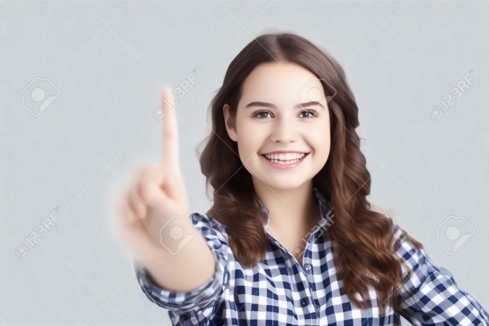 Happy cheerful student girl touching glass board with finger. Young woman in casual checked shirt standing isolated over white background. Advertising or technology concept