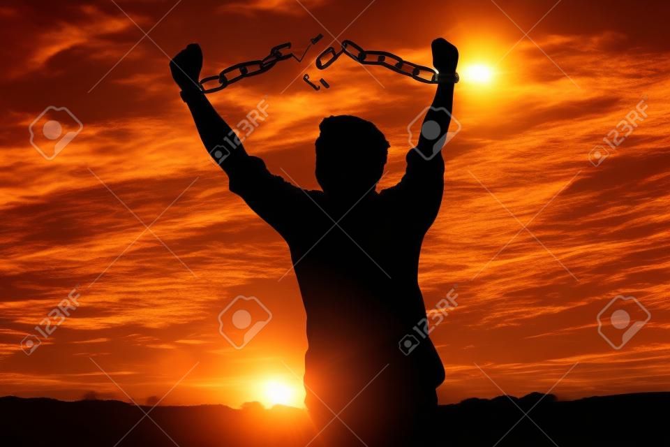 Imagen de silueta de un hombre de negocios con cadenas rotas en puesta de sol