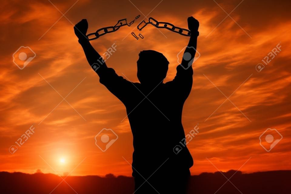 Silhouette image of a businessman with broken chains in sunset