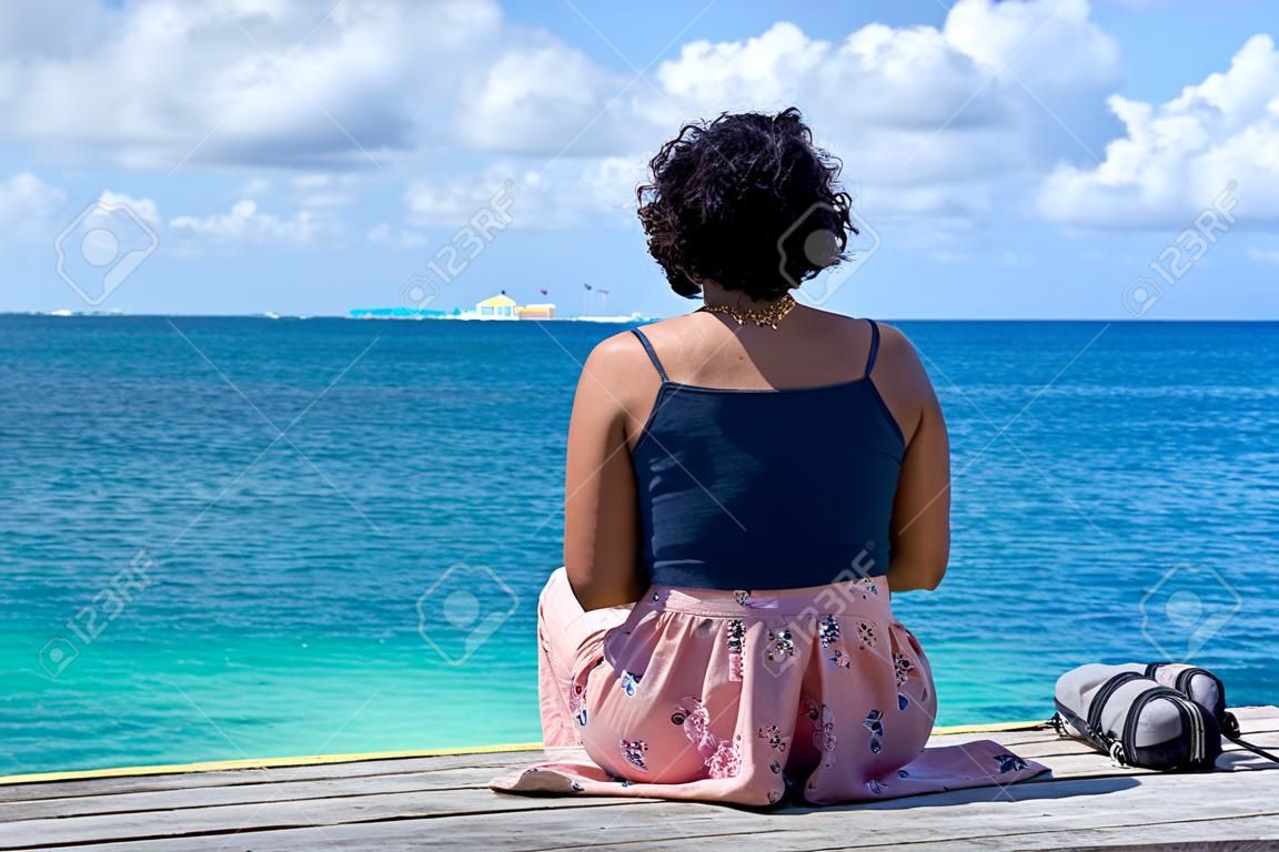 Einsame Frau sitzt am Pier / eine Frau schaut auf das karibische Meer in Mexiko