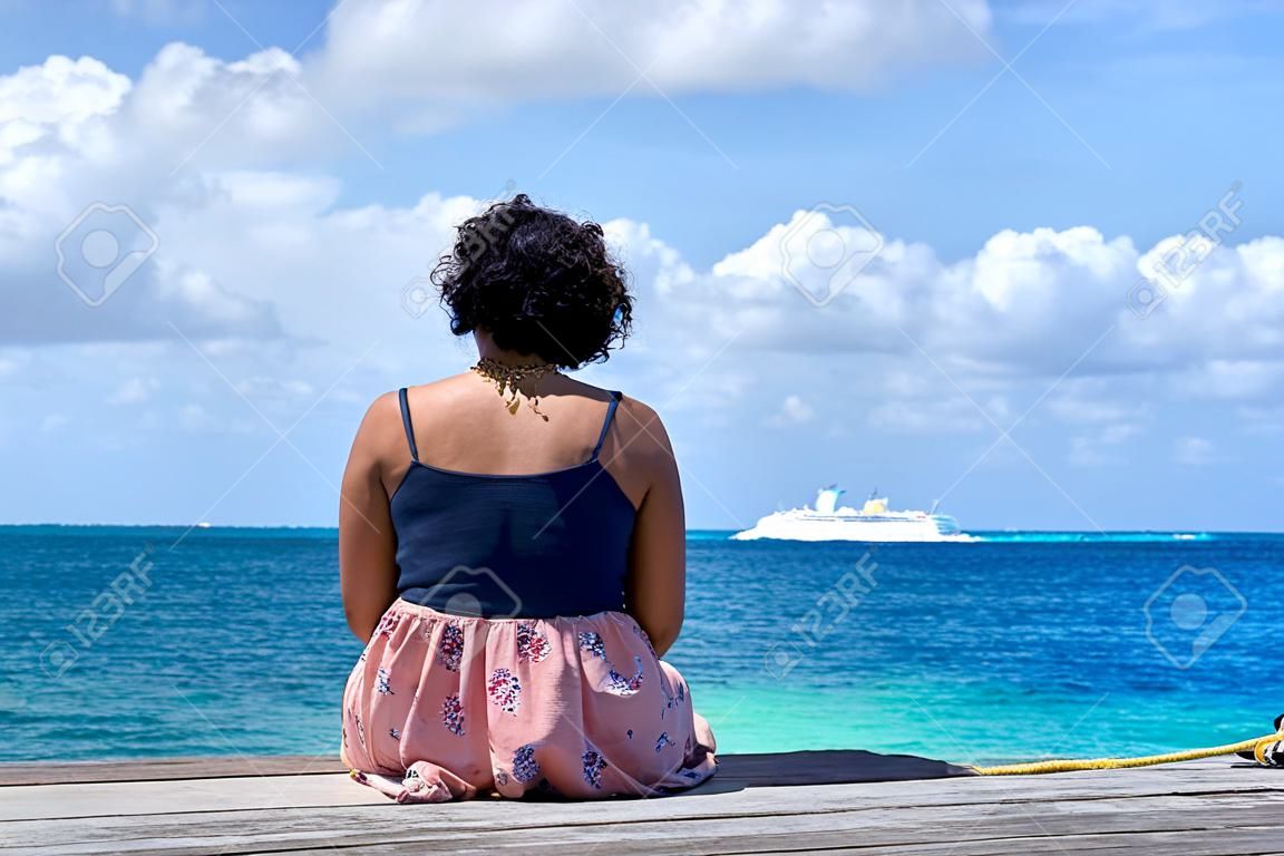 Einsame Frau sitzt am Pier / eine Frau schaut auf das karibische Meer in Mexiko