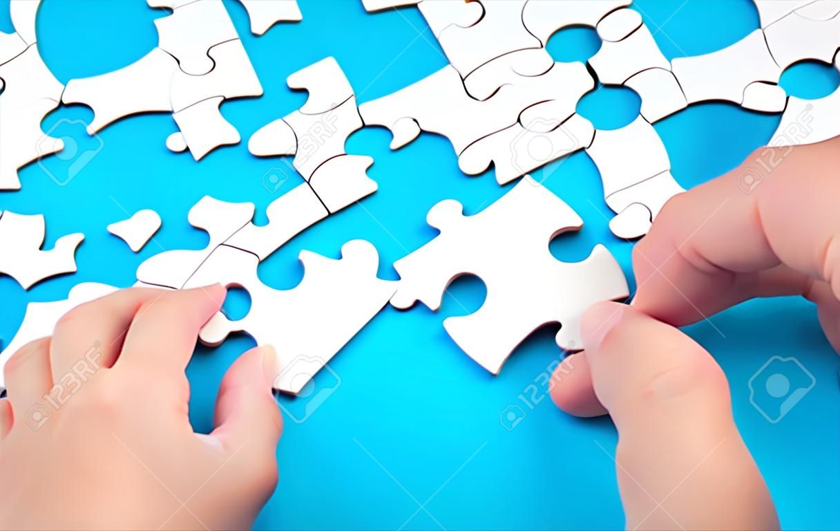 Hand putting piece of white jigsaw puzzle on blue background. Team business success partnership or teamwork.