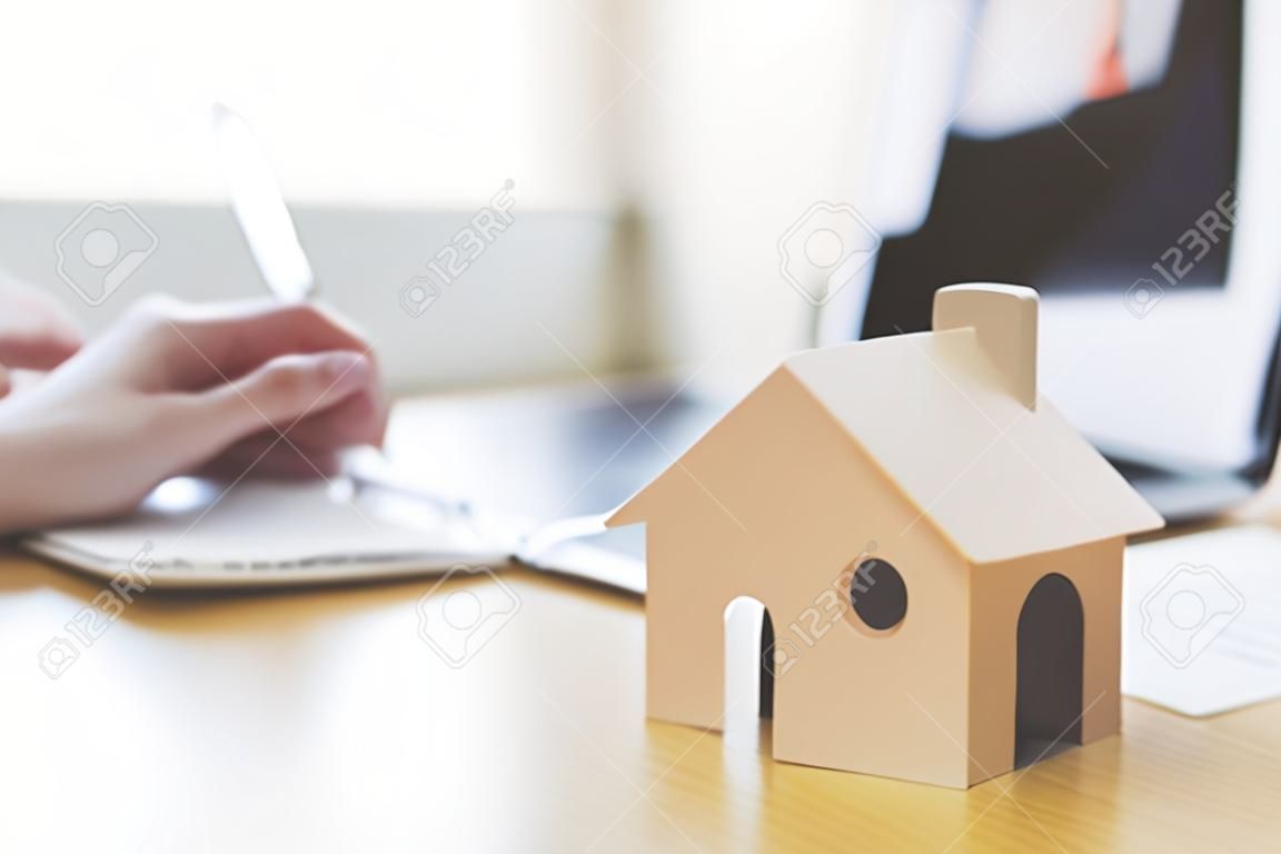 Drewniany model domu i klucz dom na drewnianym stole z ręcznym podpisaniem dokumentu umowy pożyczki lub inwestycji hipotecznej nieruchomości