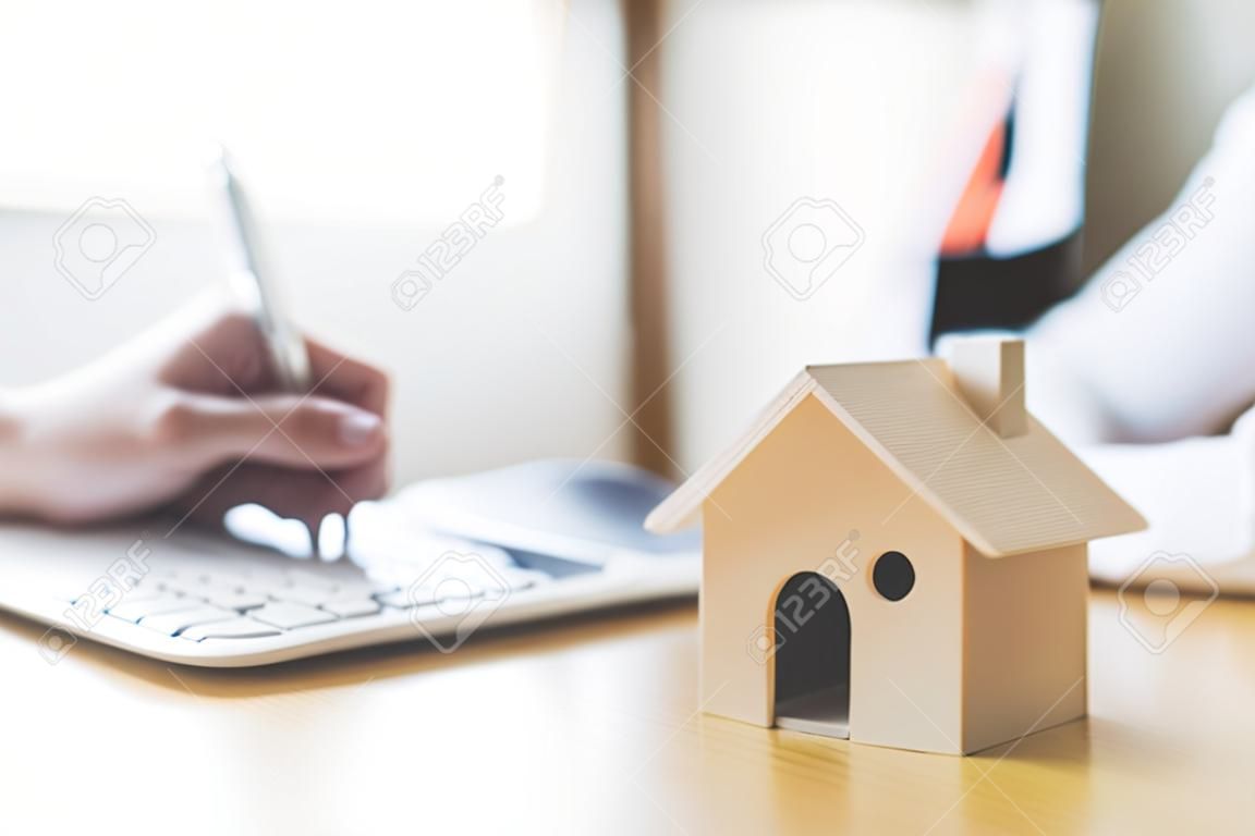 Modelo de casa de madera y casa clave en mesa de madera con firma manual del préstamo de contrato de documento o inversión de propiedad hipotecaria